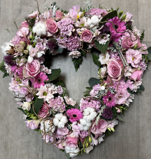A heart shaped floral tribute with the centre removed, flowered around the outline with roses, gerbera, hydrangea, lisianthus, freesia, cotton and other mixed dusty pink shades with silver foliages to complement. 